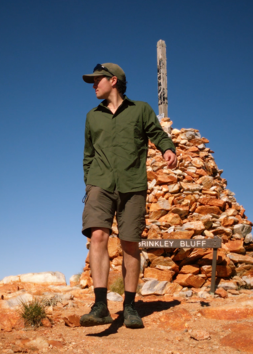 A man wearing an olive green long-sleeve Sun Ray sun shirt, under a clear blue sky.